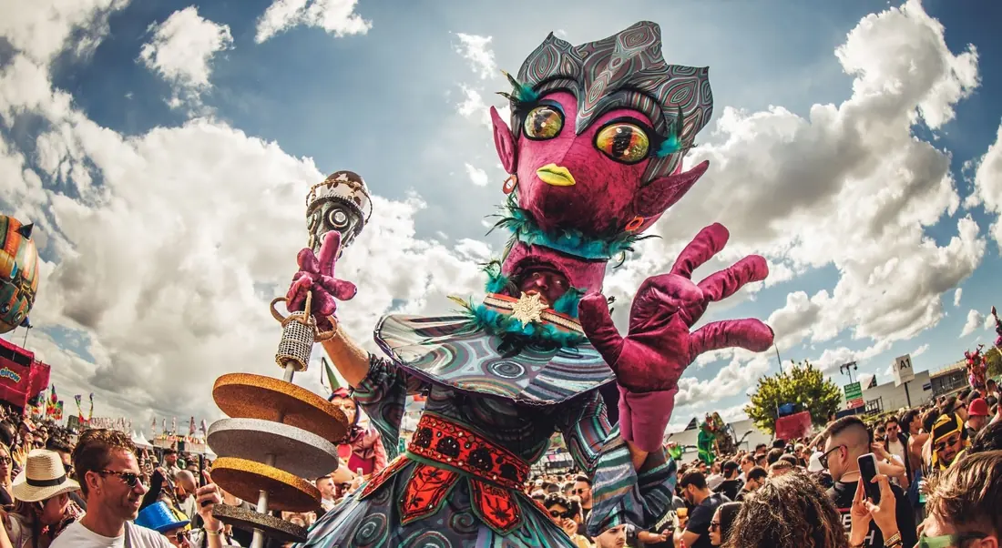 Marioneta gigante de Elrow XXL entre el público bajo un cielo de nubes